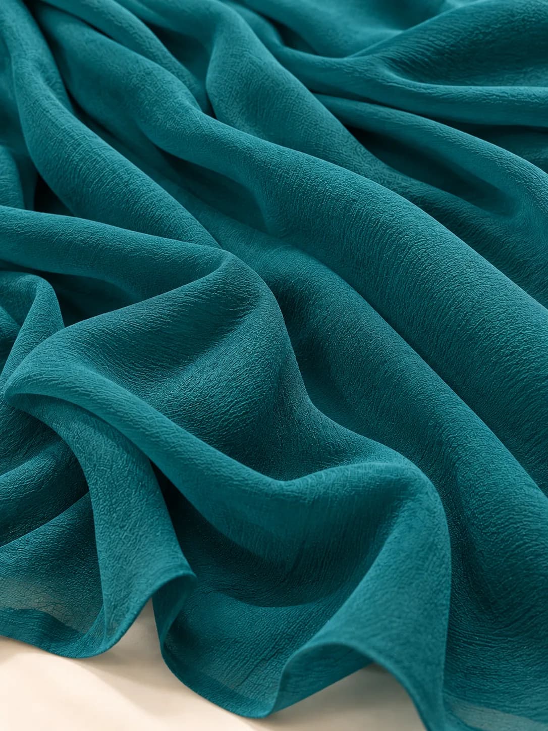 Teal georgette fabric showing its crinkled, grainy surface and fluid drape